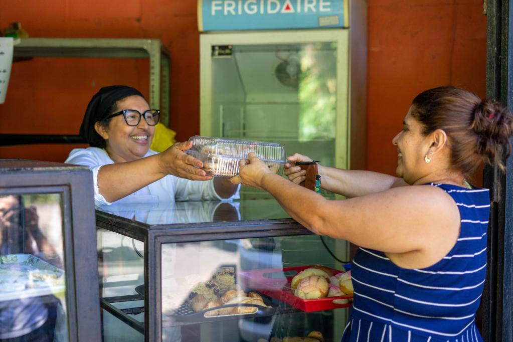 Fotografía en la que aparece Morena Cervellón vendiendo pan a una mujer que visita su negocio