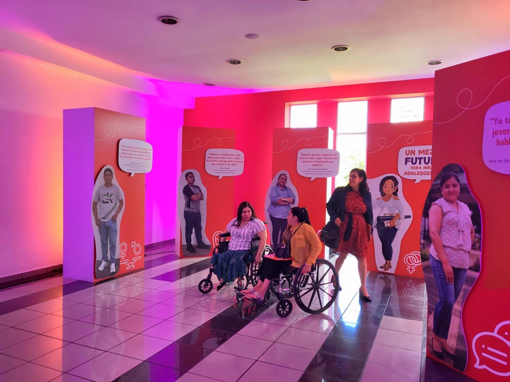 Dos mujeres con discapacidad física miran la exposición fotográfica de la Iniciativa Llegar a cero 