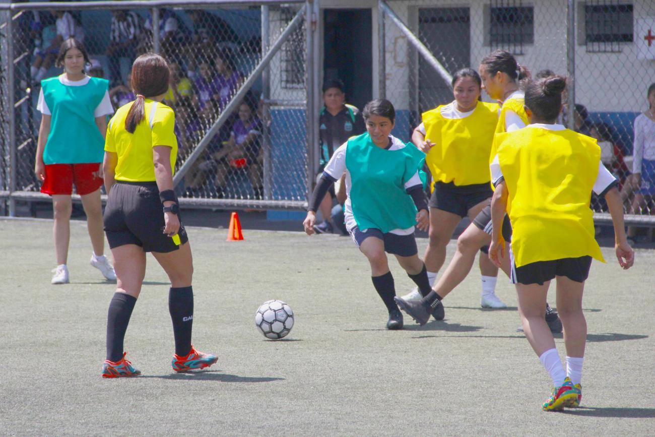 Una niña domina una pelota de fútbol sorteando la marce de otras tres niñas, mientras la árbitro sigue la jugada en el torneo deportivo que se jugó durante el día de la niña.