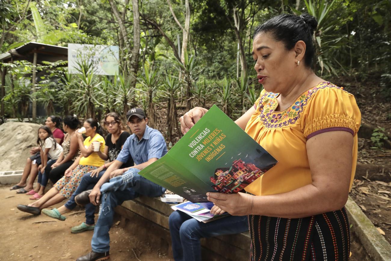Betty Pérez, una mujer indígena en primer plano, leyendo un libro a jóvenes en una reunión del Observatorio