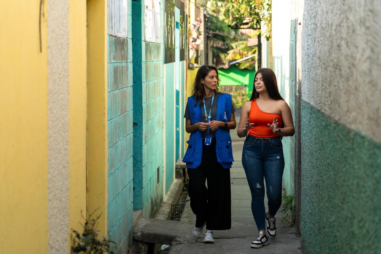 Fotografía de Saraía conversando con una funcionaria de ACNUR entre los pasajes de su comunidad en Mejicanos.