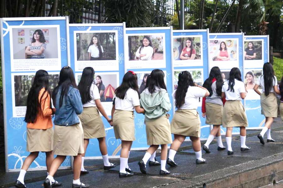 Niñas circulan en fila frente a la exposición fotográfica con testimonios sobre cómo las niñas manejan su salud mental.