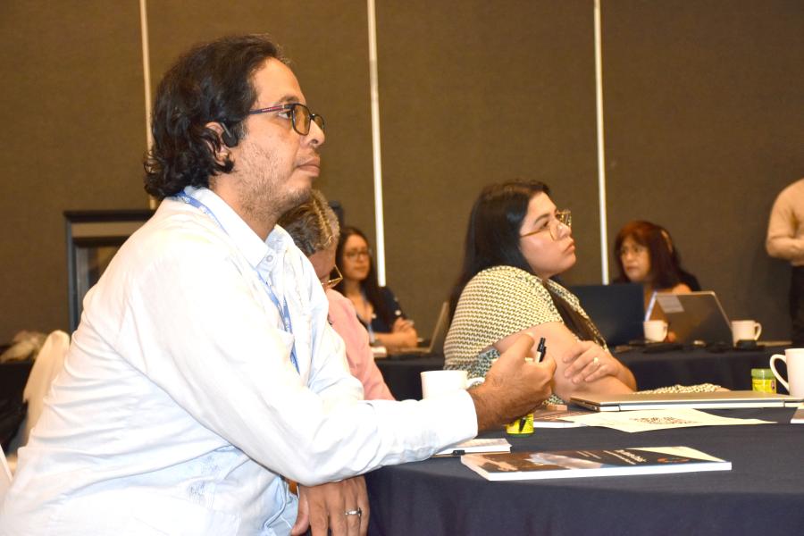 Un partipante hombre en primer, al fondo dos mujeres, toos escuchando con atención las ponencias del diálogo centroamericano