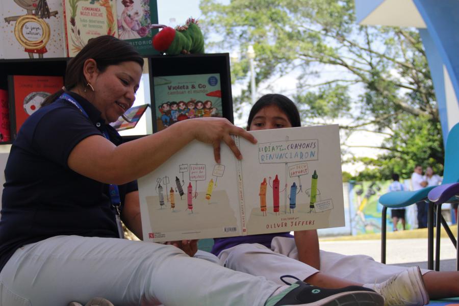 Una niña con una señora leen el libro "El día que los crayones renunciaron" en la feria interactiva que se instaló en la conmemoración del Día de la niña.