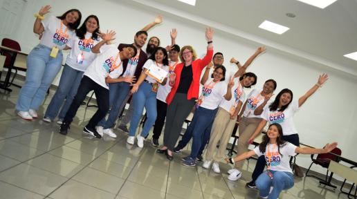 Foto de un grupo de jóvenes, mujeres y hombres, salundando alegres a la cámara, en un salón y con la representante del UNFPA al centro.