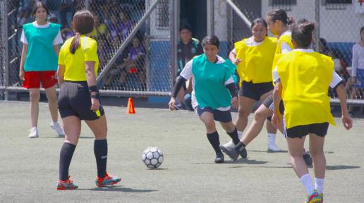 Una niña domina una pelota de fútbol sorteando la marce de otras tres niñas, mientras la árbitro sigue la jugada en el torneo deportivo que se jugó durante el día de la niña.