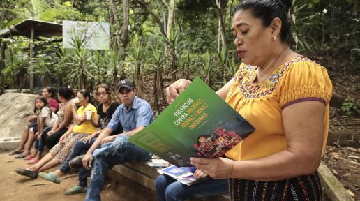 Betty Pérez, una mujer indígena en primer plano, leyendo un libro a jóvenes en una reunión del Observatorio