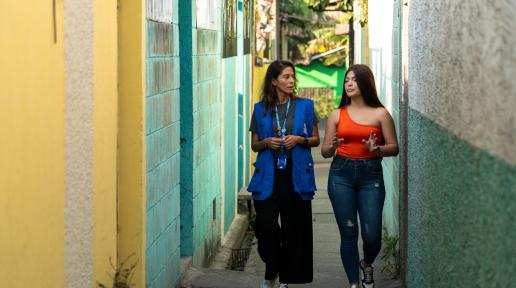Fotografía de Saraía conversando con una funcionaria de ACNUR entre los pasajes de su comunidad en Mejicanos.